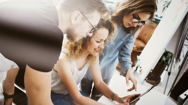 Grupa młodych dorosłych wspólnie analizujących treści na tablecie podczas pracy zespołowej w nowoczesnym biurze